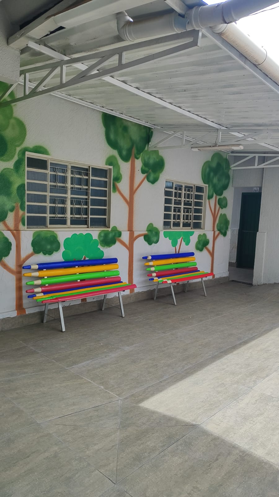 Corredor com bancos em forma de lápis coloridos e paredes pintadas com árvores